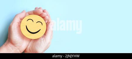 Hand holding happy smile face on blue background, Positive thinking, Mental health, World mental health day concept Stock Photo