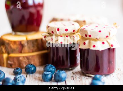Blueberry jam placed in small glasses on wooden desk. Fresh blueberries around. Homemade marmalade, concept of healthy cooking. Stock Photo