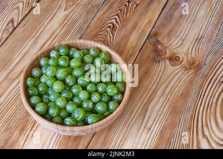 Ripe green gooseberries in bowl on wooden table. Harvest of the berries. Stock Photo