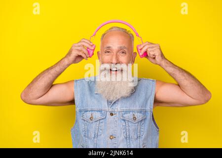 Photo of handsome excited retired guy wear jeans waistcoat listening headphones isolated yellow color background Stock Photo