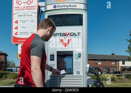 Young man using an electric vehicle chargepoint operated by Instavolt, a company owning a nationwide network of electric vehicle chargepoints, They announced price increases to 66p per kwh due to energy price crisis in summer 2022. Stock Photo