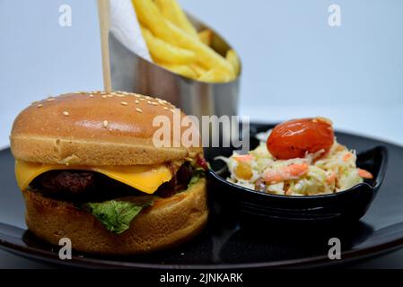 fast food menu. hamburger, french fries and salad. burger with beef stake, cheese and pickle. mayonnaise ketchup mustard on the  plate. Stock Photo