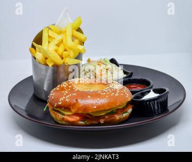 fast food menu. hamburger, french fries and salad. burger with beef stake, cheese and pickle. mayonnaise ketchup mustard on the  plate. Stock Photo