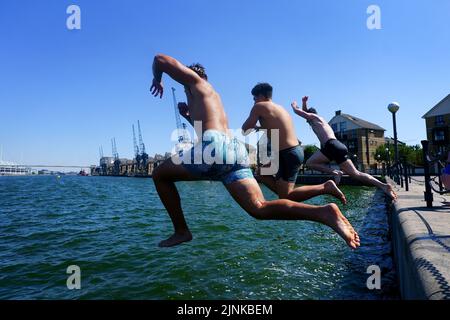 Three young men jump into Royal Victoria Dock in east London. A drought is set to be declared for some parts of England on Friday, with temperatures to hit 35C making the country hotter than parts of the Caribbean. Picture date: Friday August 12, 2022. Stock Photo