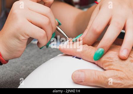 Close-up of the hands of two unrecognizable women, one young and one old, having a manicure. The young woman is applying gel with a brush with an oran Stock Photo