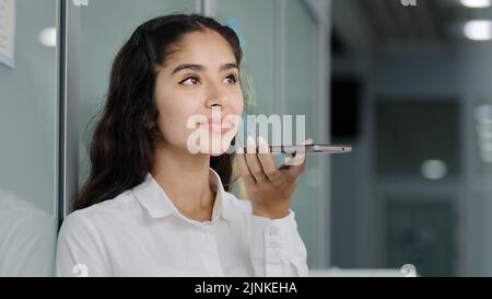Young indian businesswoman talks on speakerphone answers business call records audio message woman manager sends voicemail using virtual assistant Stock Photo