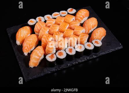 Big set of sashimi rolls with salmon, rolls California and Maki on a black flat board. Concept of delivery of delicious original sushi sets. Stock Photo