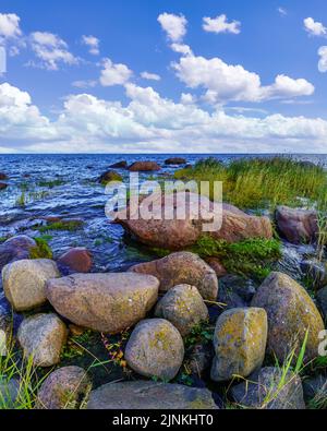 Seascape with large rocks on the shore and white clouds over blue sky. Stock Photo