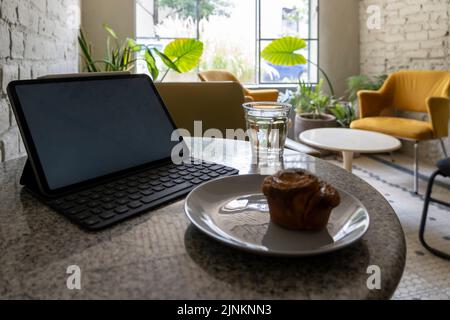 pancake or cupcake on ceramic plate, terrazzo table, tablet in the back. Enjoying sweet bread while working Stock Photo