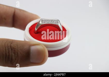 Engagement ring in a box, Silver ring in a small red jewelry box held in hand on white background Stock Photo