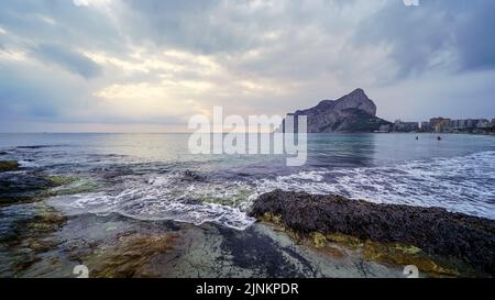 Panoramic landscape in the sea with a large mountain on the horizon and waves breaking against the rocks. Stock Photo