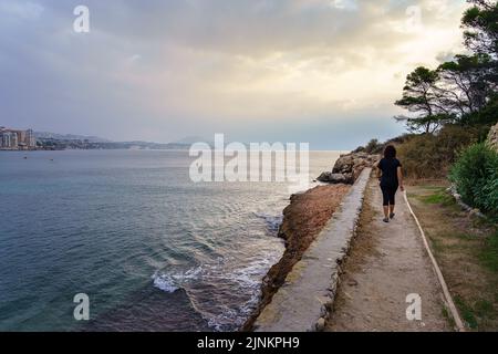 Woman walking along the sea cliffs at sunset on a summer day. Stock Photo