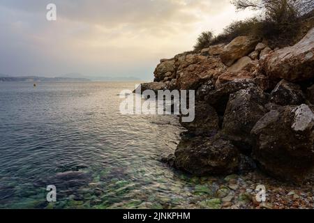 Stony beach next to the cliff rocks on a golden sunset. Stock Photo