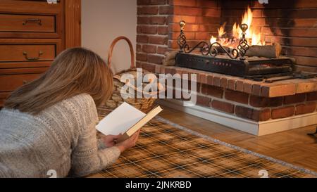 Woman lying on the floor on a blanket in front of the comfortable warmth of a fireplace. Stock Photo