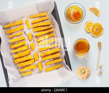 Autumn food. Baked pumpkin slices with cinnamon and honey on a baking sheet with tea and dried fruits on a blue background. Vegan dessert, healthy foo Stock Photo