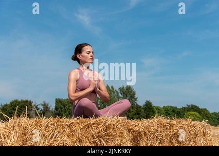 Woman sitting on a hay bale in the countryside and meditating. Yoga concept. Stock Photo