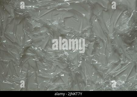 Wrinkled plastic wrap on gray color background. Crumpled transparent plastic cellophane. Reflecting light and shadow on creases and folds in plastic Stock Photo