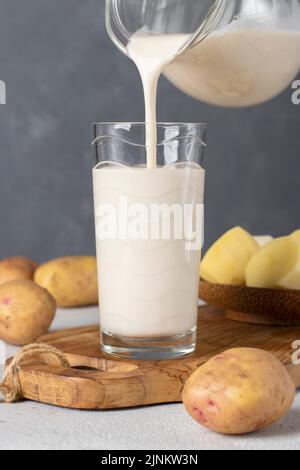 Vegan potato milk is poured into a glass from a jug. Use of plant-based and lactose-free milk replacer Stock Photo