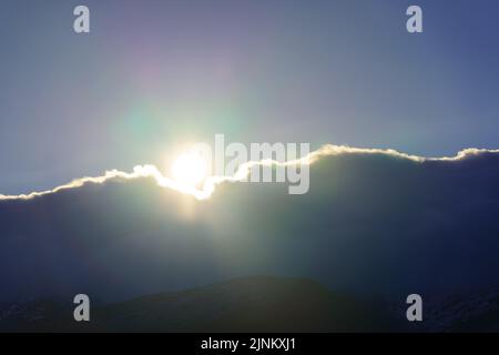 Landscape background with sun rising through the clouds in the high mountains. Stock Photo