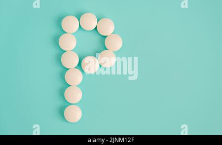 Letter P made from white pills on a blue background. White medical pills. Macro top view with copy space. Health care and pills concept, pharmaceutica Stock Photo