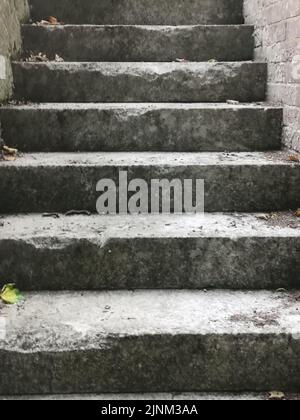 Old weathered, worn concrete outdoor staircase with brick wall to side Stock Photo