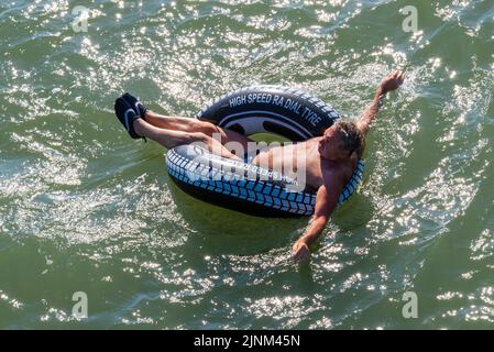 Southend on Sea, Essex, UK. 12th Aug, 2022. The hot weather has continued in the new seaside City of Southend on Sea, with many people heading to the resort to cool down by the sea. White Caucasian male floating in a rubber ring Stock Photo