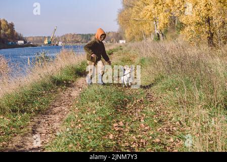 Kid playing with dog walking at rustic promenade along canal on nice Fall day Stock Photo