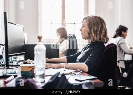 Yound devoted female software developers team working on desktop computer in IT statup company. Stock Photo