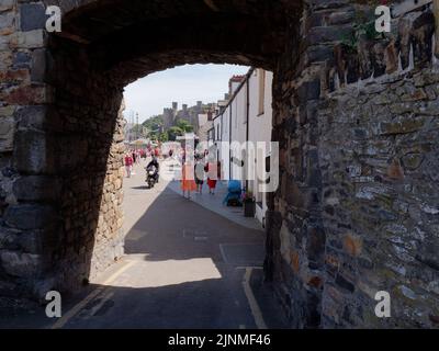 Conwy, Clwyd, Wales, August 07 2022: People walking near the town walls with a castle in the background Stock Photo