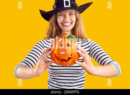 Small decorative pumpkin with funny face carved in Halloween style in hands of cheerful woman. Stock Photo