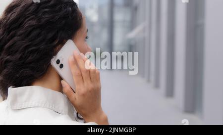 Back view unrecognizable boss manager businesswoman with curly hair lady in formal shirt standing outdoors talking mobile phone call remote chatting Stock Photo