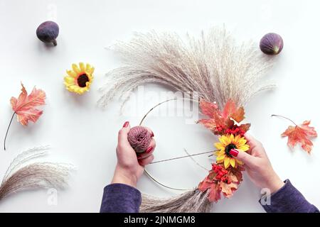 Floral wreath from dry pampas grass and Autumn leaves. Hands tie decorations to metal frame. Stock Photo