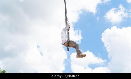 Worker without protective gear swinging on the crane chains. Bad example of work safety. Dangerous working style Stock Photo