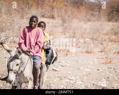 Botswana Africa - August 28 2007; Two young local men riding donkey in dry African landscape Stock Photo