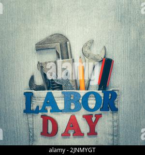Worn and weathered blue jeans with work tools in the pocket and Labor Day text, celebrating American workers. Stock Photo