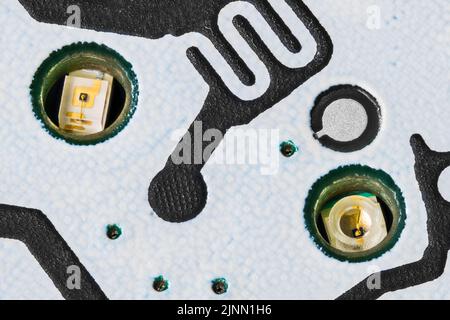 Closeup of small LED diodes inside white printed circuit board. Electronic light emitting sources for mobile phone keypad buttons backlighting on PCB. Stock Photo