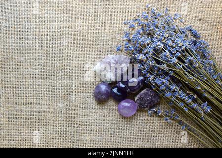 Beautiful amethyst stones and amethyst druze with a dry bouquet of lavender against a background of coarse burlap fabric. Magic amulets. Сopy space Stock Photo