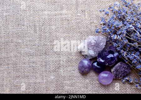 Beautiful amethyst stones and amethyst druze with a dry bouquet of lavender against a background of coarse burlap fabric. Magic amulets. Сopy space Stock Photo