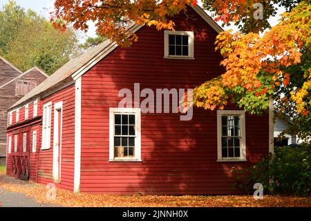Fall foliage and colorful leaves surround a small red house on a vibrant autumn day in New England Stock Photo