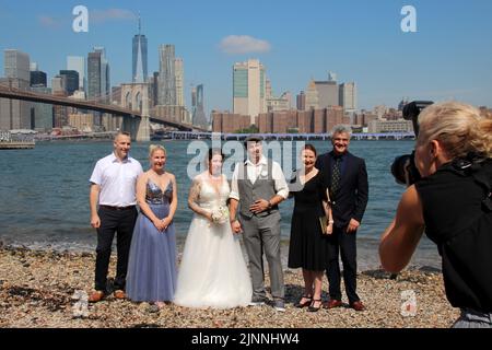 New York, USA. 02nd Aug, 2022. Wedding planner Erol Inanc (2nd from right) stands together for a group photo on the sidelines of the wedding ceremony of Annika Heisig (3rd from left) and Patrick Brosch (4th from left), as well as the registrar (3rd from right) and the witnesses at Pebble Beach in Brooklyn Bridge Park. The Munich native has been working as a wedding planner in New York for more than 14 years and fulfills wedding wishes from Brooklyn to Times Square. (to dpa 'Perfect moment': German fulfills wedding dreams in New York') Credit: Christina Horsten/dpa/Alamy Live News Stock Photo