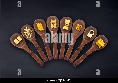 Wooden cooking spoons filled with various types dry pasta isolated on a black background Stock Photo
