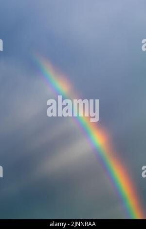 The sun's rays shine on a multi-colored rainbow from behind the clouds. Vertical photo Stock Photo