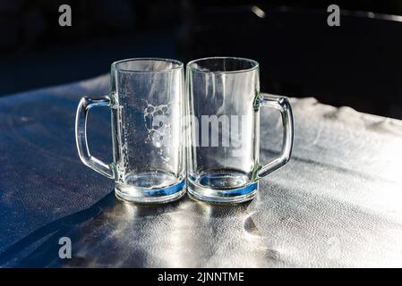 Empty beer two mugs after party on black table at bar table.Two drunk empty beer glasses.Closeup. Stock Photo