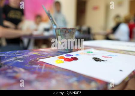 Paint brushes in glasses and colourful paints on white sheet of paper Stock Photo