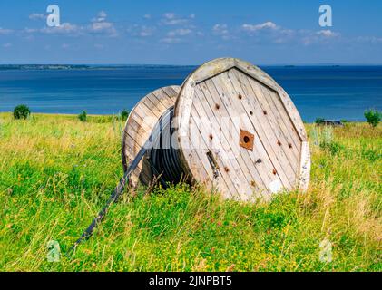 Black wire electric cable on wooden spool. Wooden reels with electrical power cables at the edge of the sea. Wire on wooden coil. Electrical power wire equipment Stock Photo