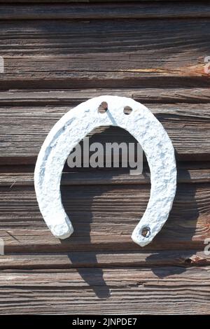 An old horseshoe hangs on a log wall. Painted white. Close-up. Stock Photo