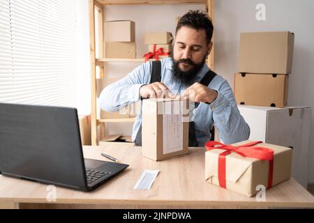 a man sticking a barcode on a cargo on his desk. A person working in a dropshipping office prepares a package for delivery to a customer. SME Stock Photo