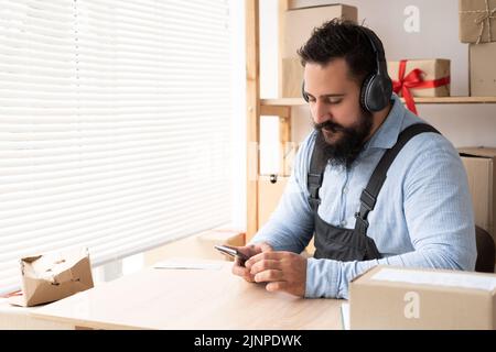 Indian businessman listening to music by headphones and smartphone while working in working space. Freelance or digital nomad lifestyle Stock Photo