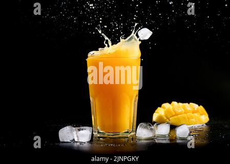 Fresh mango juice. A splash of mango cocktail on a black background. Ice cubes fall into the mango juice. Stock Photo
