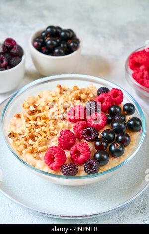 Oatmeal with raspberries, blackcurrants and crushed nuts in a glass bowl. Healthy balanced food Stock Photo